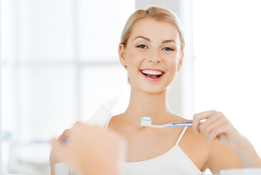 Junge Frau putzt lachend Zähne
